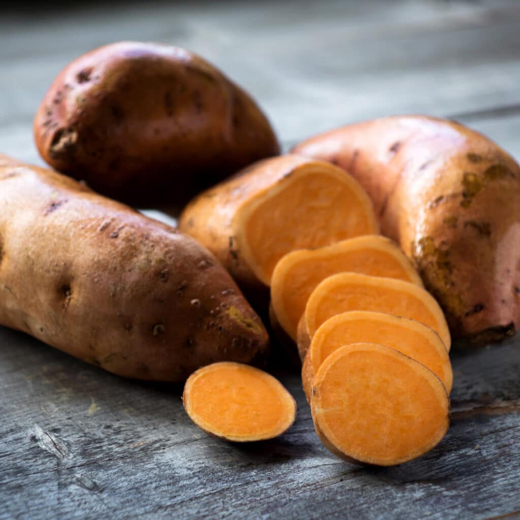 Raw sweet potatoes on wooden background closeup