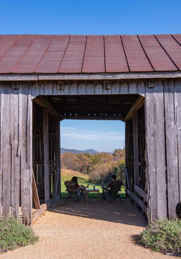 A couple drinking wine in the barn at Early Mountain Vineyards with views of fall foliage in Virginia Wine Country.